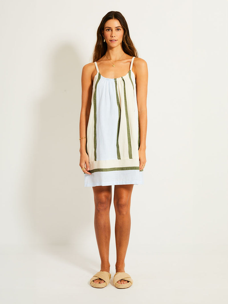 Woman Standing Wearing lemlem ZINA Dress featuring a bold asymmetrical color-block pattern, where airy light blue effortlessly blends with soft sage and cream