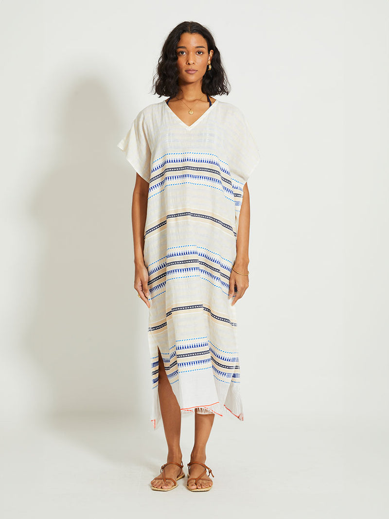 Woman Standing Wearing lemlem DALILA | V Neck Caftan featuring a soft shadow stripe base with graphic Tibeb-inspired bands in rich blues, black, and vanilla on a creamy white ground