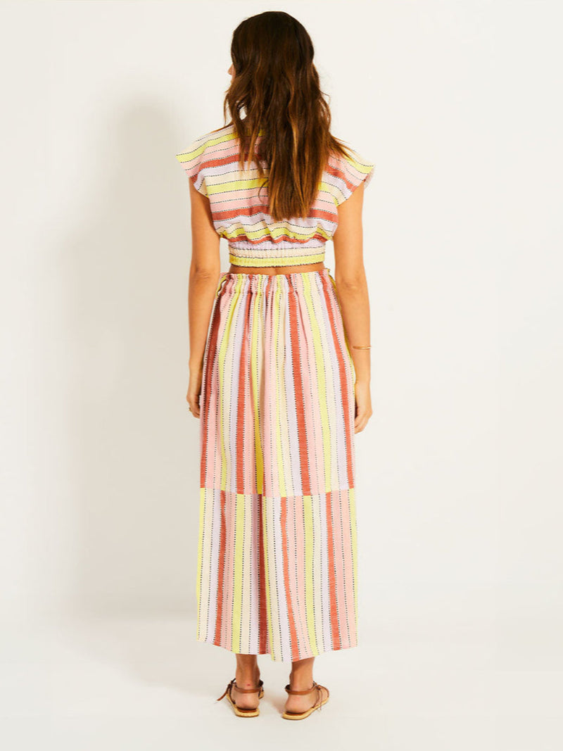 Back of a Woman Standing Wearing lemlem ALIA Plunge Top featuring soft sorbet-colored stripes in shades of peach, rust, and orchid, accented with a citrus yellow pop.
